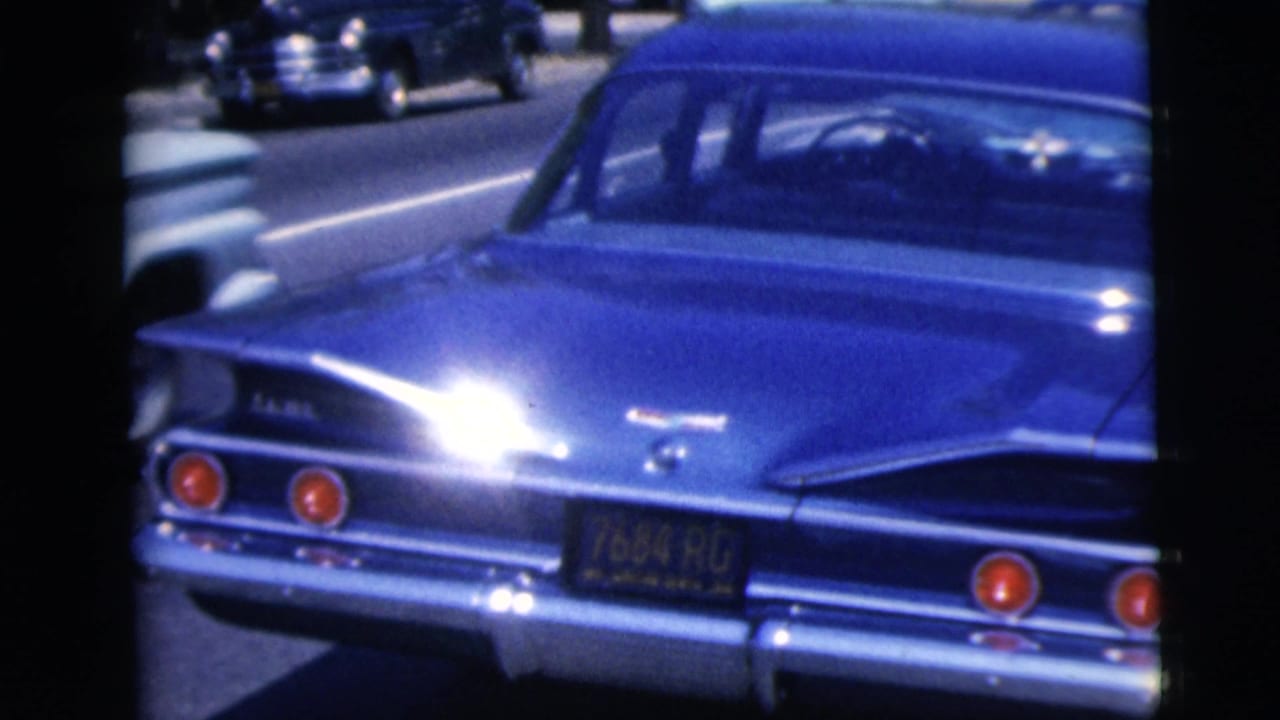 Rear view of a shiny blue 1960s car parked on a street among other vehicles.