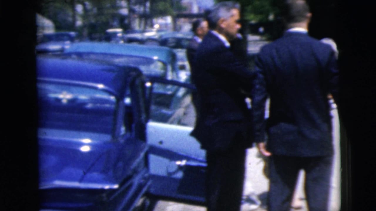 Two formally dressed men stand near an open car door in the supplied 1962 Moline home-movie footage.