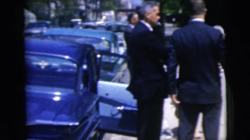Two formally dressed men stand near an open car door in the supplied 1962 Moline home-movie footage.
