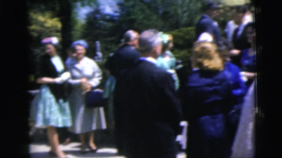 A group of adults in formal clothing gathers outdoors in Moline, Illinois, with dresses, suits, and hats visible.