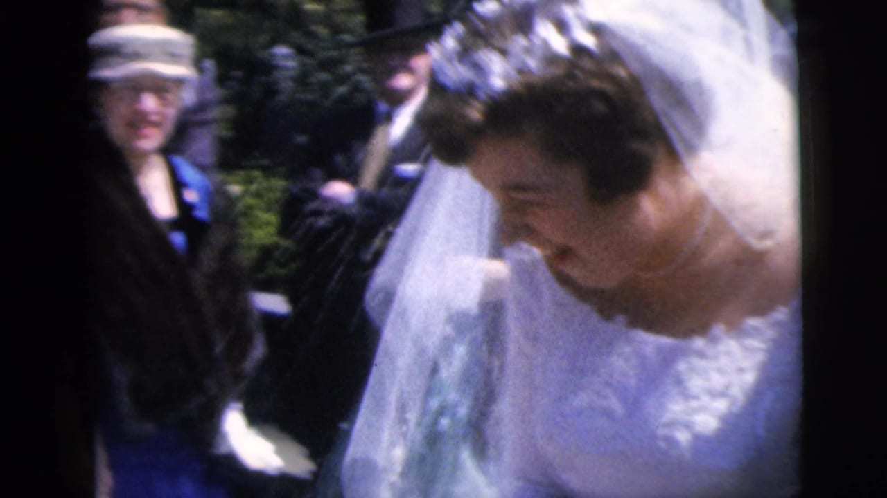 1962 Moline wedding home movie frame showing a bride in a white veil moving through guests in formal clothing.