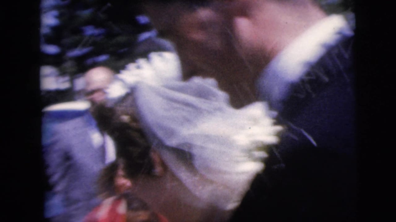 Bride and groom move close together as guests stand nearby.