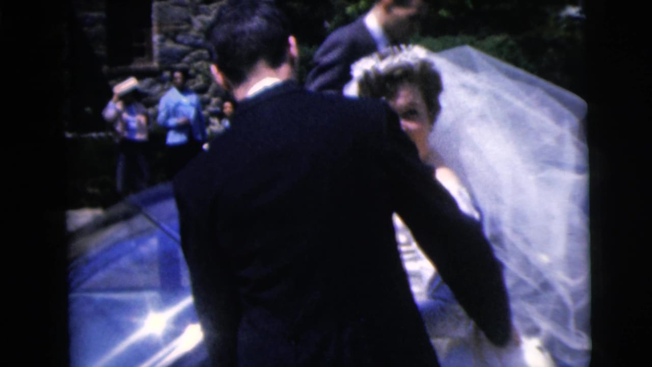 1962 Moline wedding frame with bride and groom beside a blue car while guests watch near the stone building.