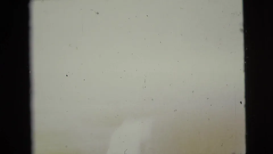 A mostly overexposed 8mm frame shows pale color, dust specks, and only faint traces of the underlying home-movie image.