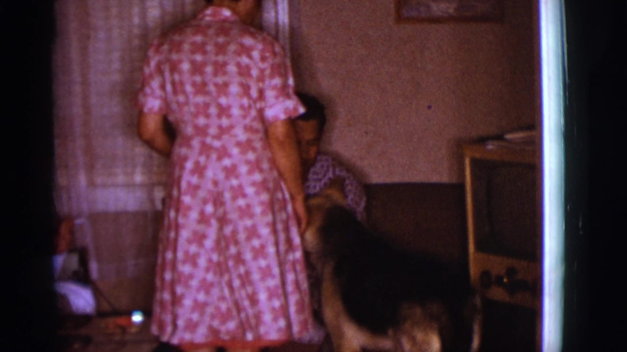 In a 1966 Clarkdale, Arizona home-movie frame, a woman in a pink patterned dress stands with her back to camera near a seated man and dog.
