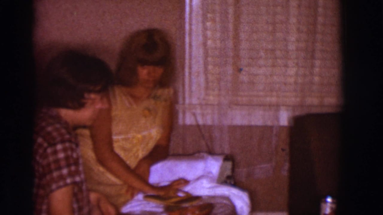 Woman in yellow dress reaches toward a small dog as a young man sits beside her.