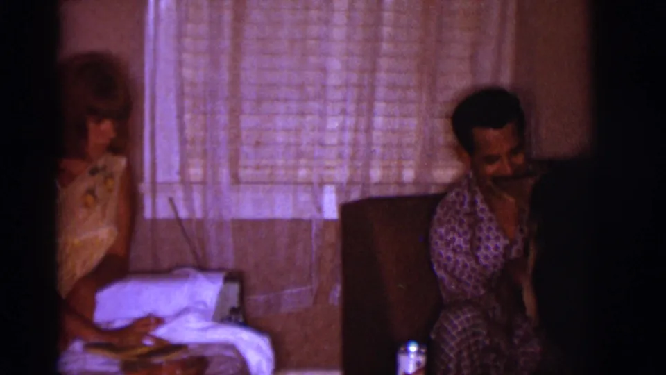 The scene shifts to a man in patterned pajamas seated near a curtained window, with the woman partly visible at left in the private interior.