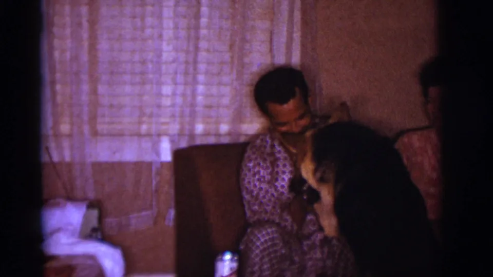 A man in patterned pajamas sits smiling near other adults in the Clarkdale home interior, with curtains and bedding visible behind them.