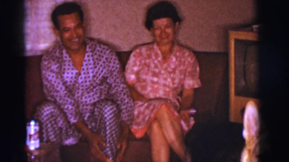 In the Clarkdale 1966 interior, the man and woman sit together on a couch with a wood-cabinet television visible at the side.
