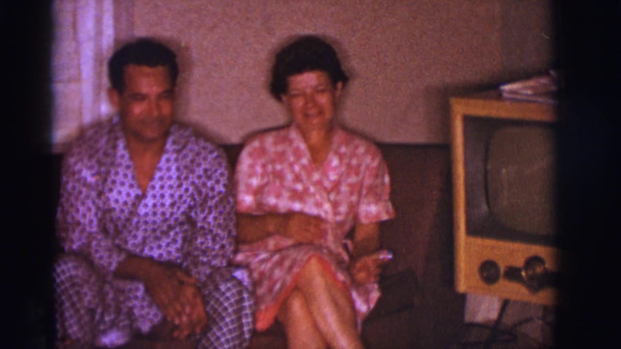 1966 Clarkdale, Arizona frame of a couple in patterned sleepwear seated together on a couch beside a wooden television set.