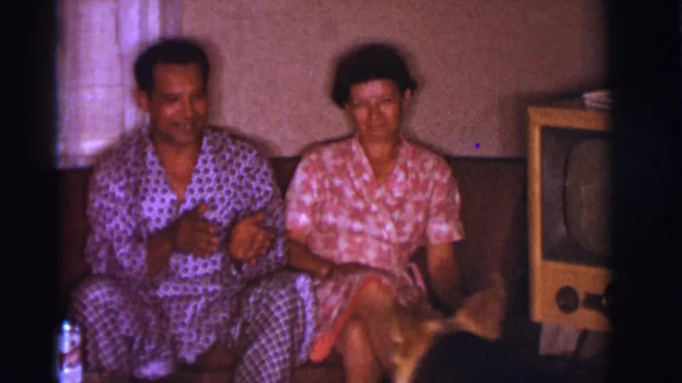 1966 Clarkdale, Arizona home-movie frame showing a couple on a couch with a dog entering near their knees in the living room.