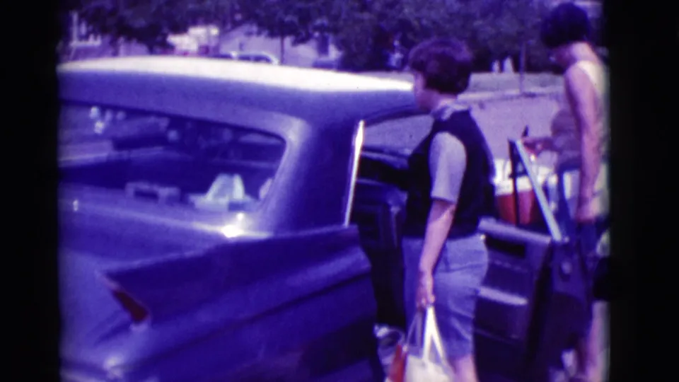 The open trunk of a classic car holds luggage while people stand beside it on a sunny Clarkdale, Arizona street in 1966.