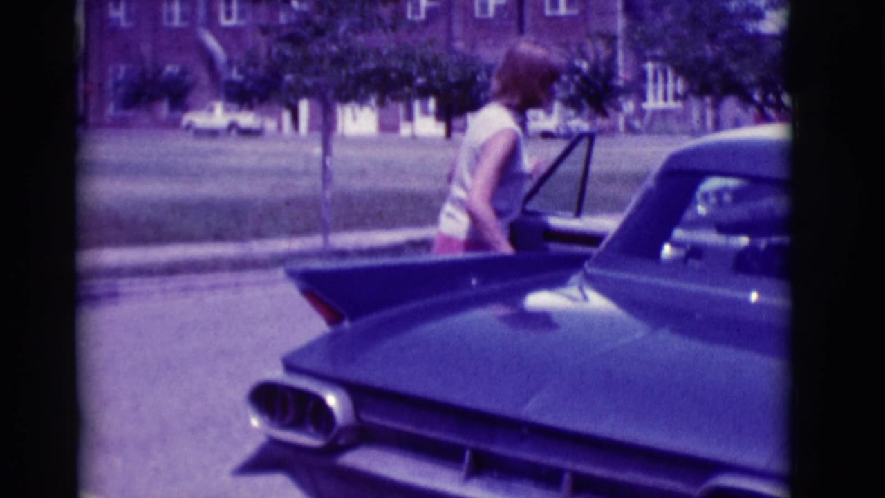 Woman in sleeveless top opens a car door beside a dark finned sedan.