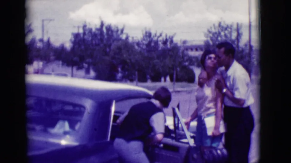 A woman leans into the back seat of a classic sedan while a man and another woman stand close by in the Clarkdale street scene.