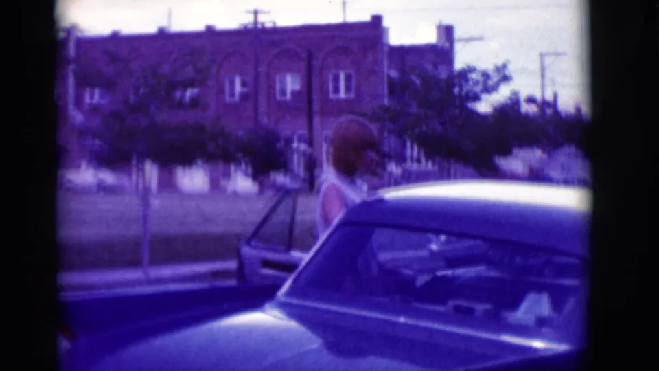 Woman by the open door of a classic car, with a brick building and roadside trees visible in Clarkdale, Arizona.