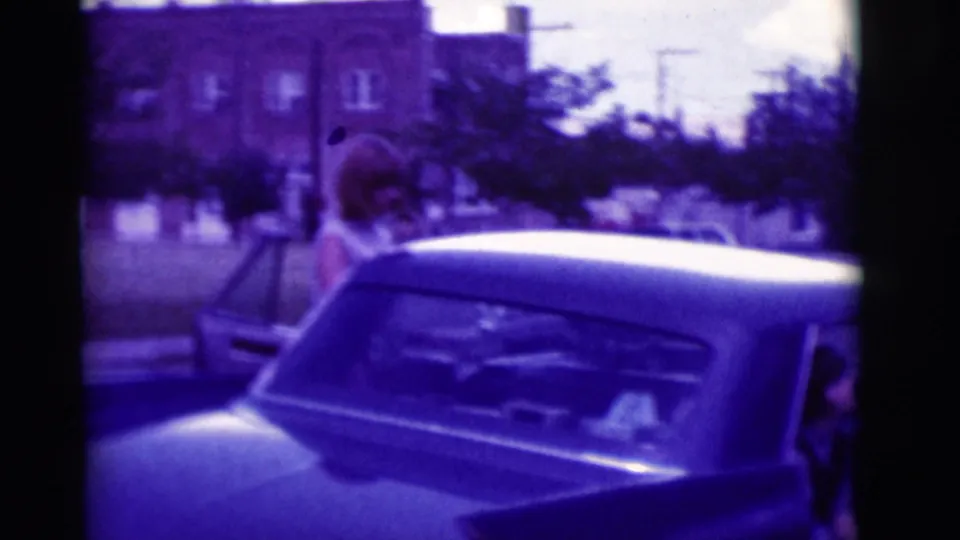 Rear-side view of the classic car in the 1966 Clarkdale home movie, with a woman near the open door.