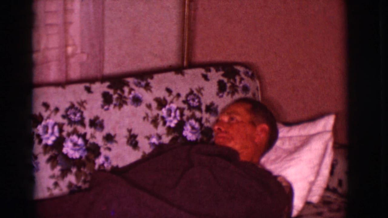 Adult man lies under a dark blanket on a floral sofa with a white pillow.