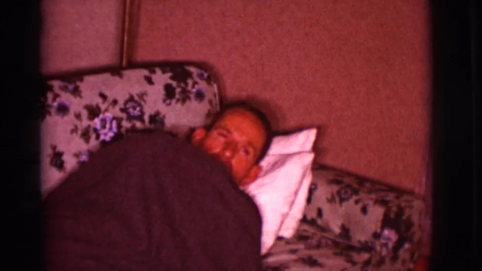 At the end of the 1966 Clarkdale home-movie moment, the man turns his face toward the camera from the couch.