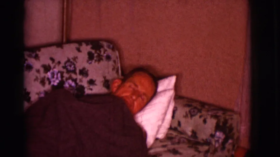 A closer view shows the man lying on the floral couch with a white pillow behind his head in the 1966 home-movie footage.