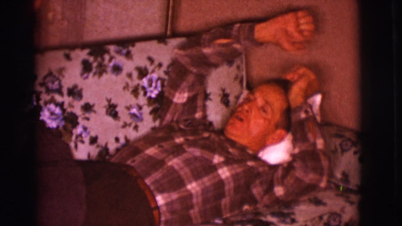 Man in plaid shirt lying on a floral couch with one arm raised.