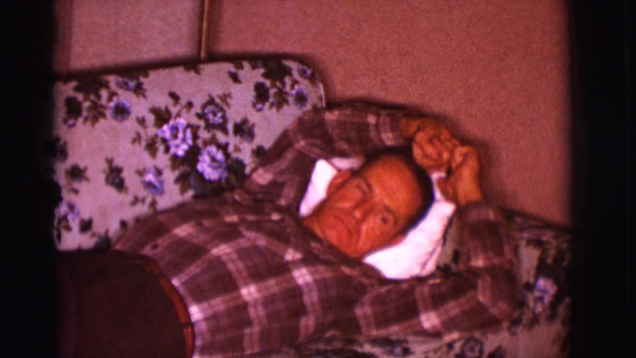 Man lying on a floral couch with both arms near his head.