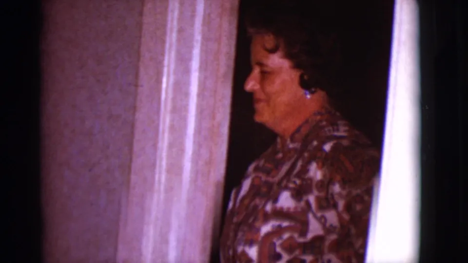 A woman in a patterned blouse smiles from a doorway in the Clarkdale home interior, facing slightly toward the camera.