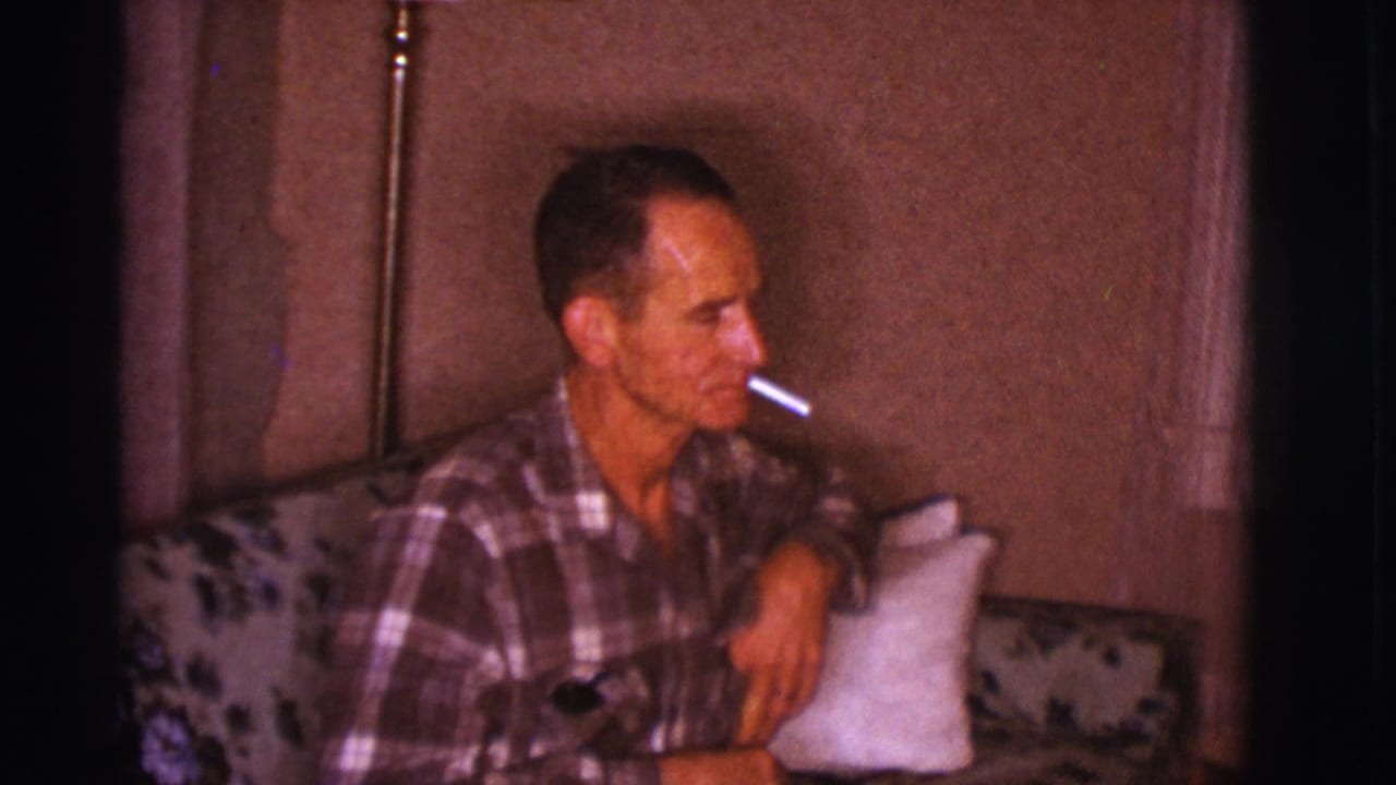 Man sits back on the couch with a cigarette, one arm resting near a pillow.