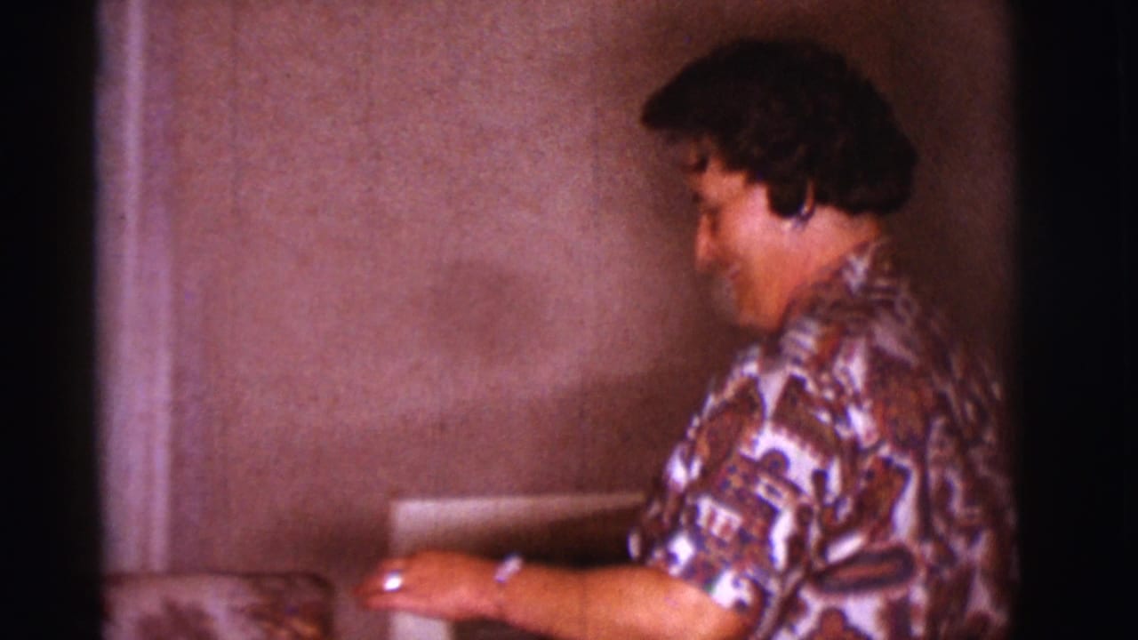 Woman in patterned blouse smiling beside an interior wall.