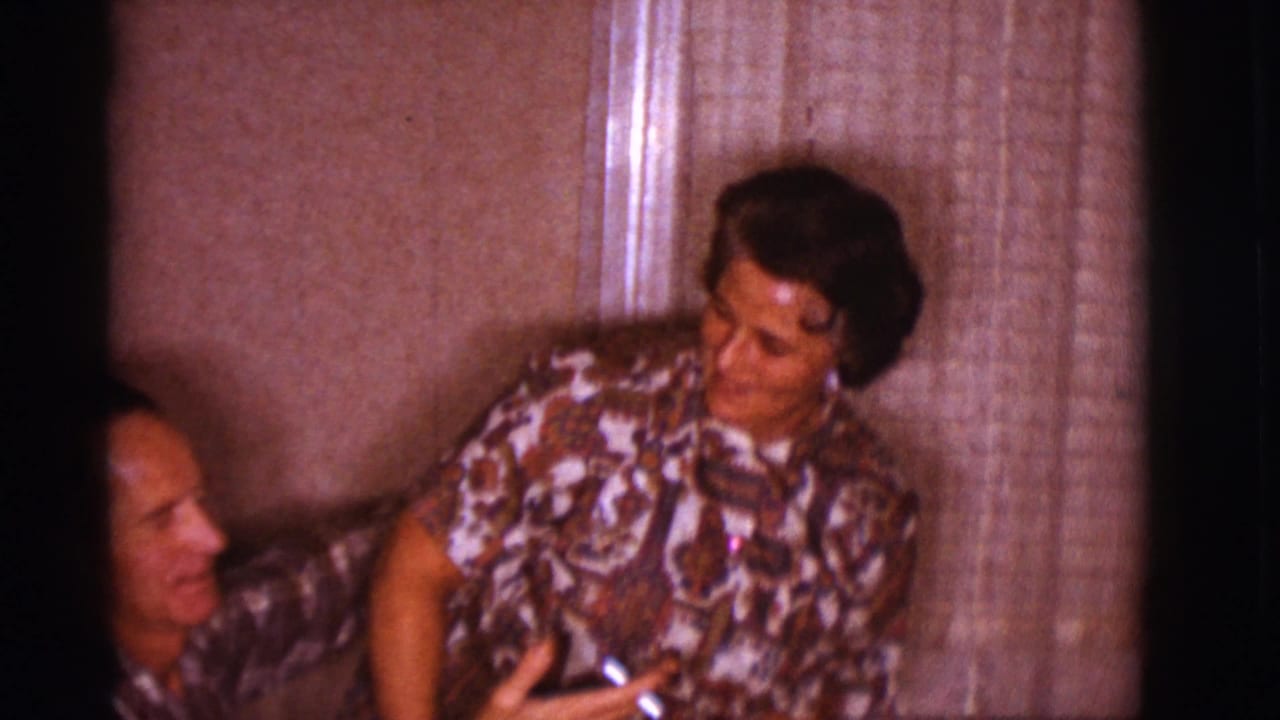 The couple sits closely on a couch in a Clarkdale living room, with the woman turned toward the man and curtains behind them.