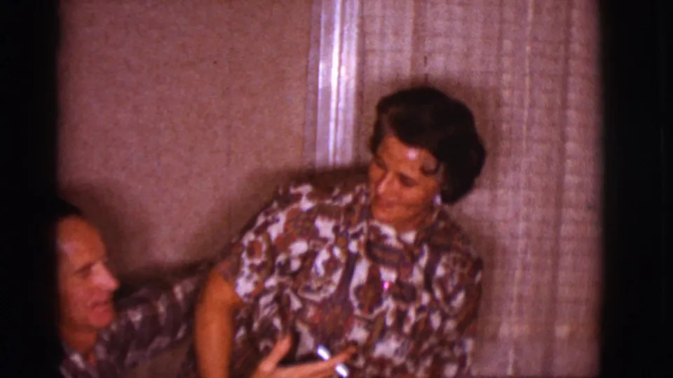 The couple sits closely on a couch in a Clarkdale living room, with the woman turned toward the man and curtains behind them.