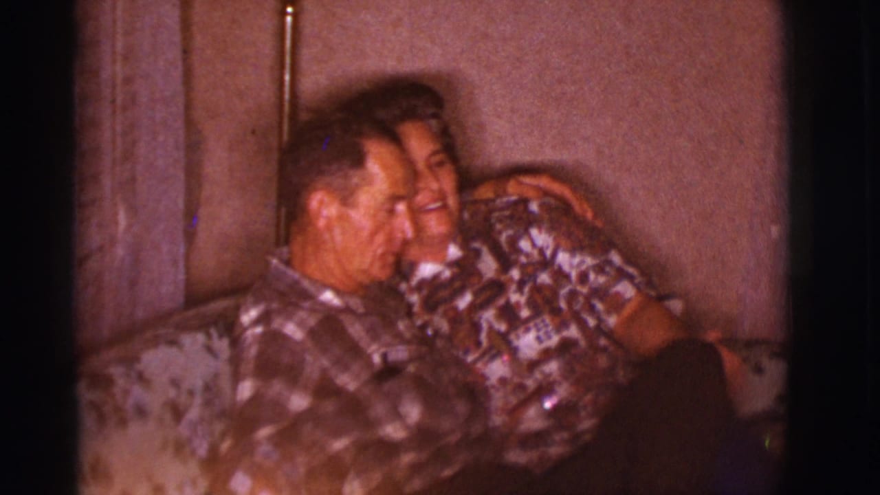 The couple embrace on a floral couch, with the woman smiling as she leans against the man in this 1966 home-movie frame.
