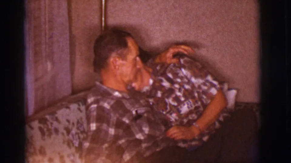 The woman rests against the man on a floral couch, showing a quiet affectionate pose in the 1966 Clarkdale home-movie footage.
