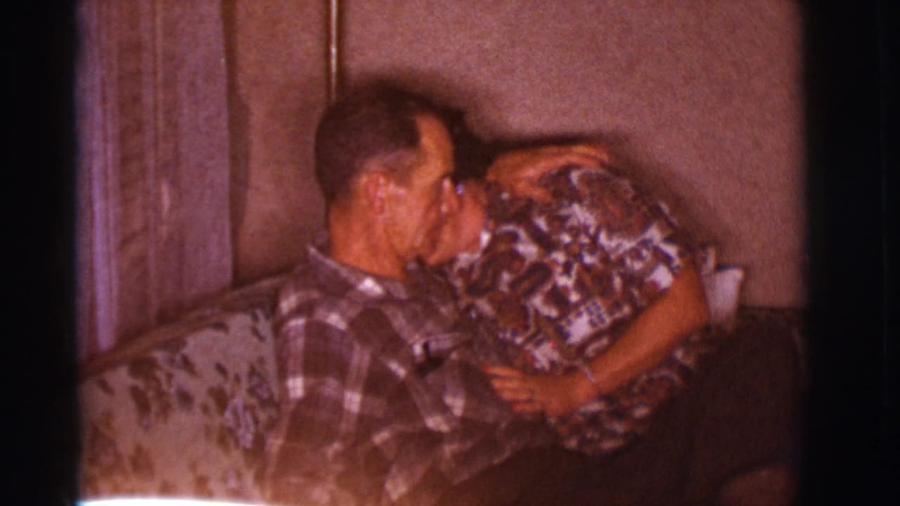 Man and woman embracing on a patterned couch inside a home.