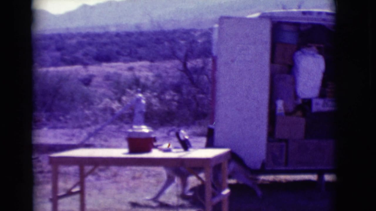 Folding table and red cooler beside an open trailer in a desert landscape.