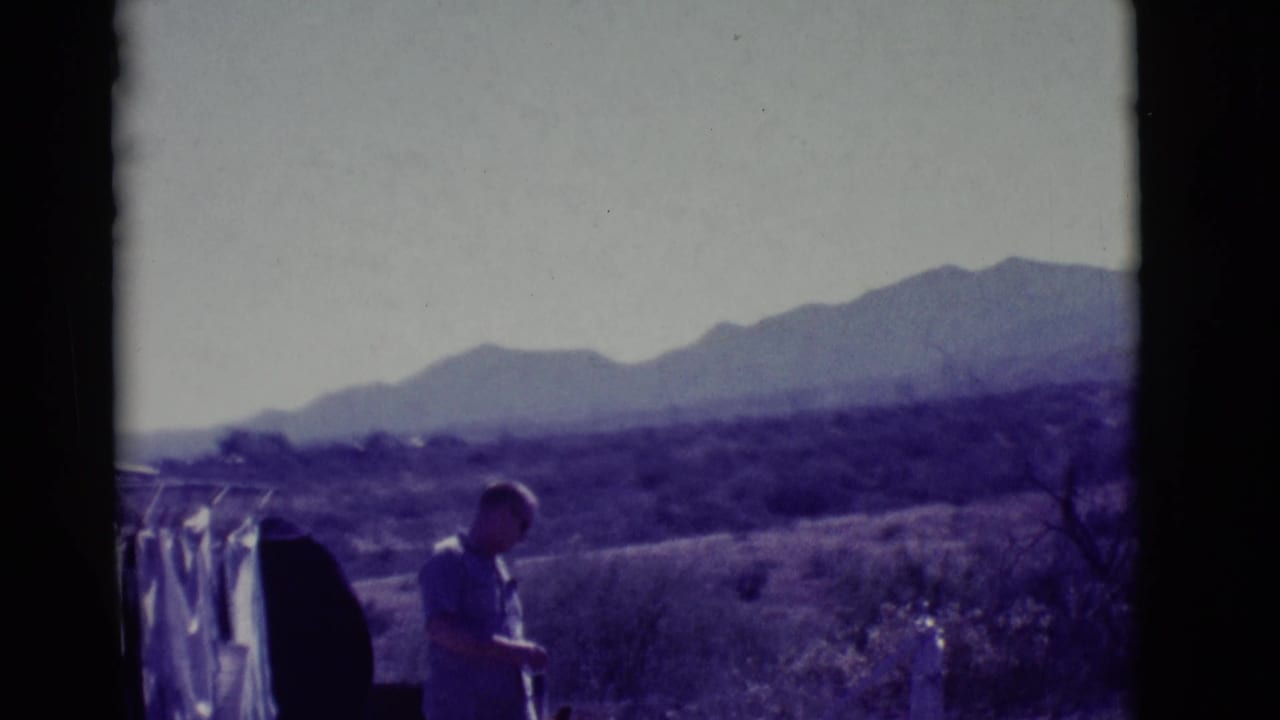 Man standing near laundry in a desert landscape with mountains in the distance.