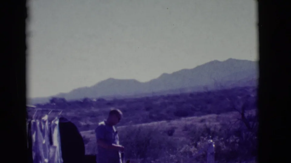 In 1966 Clarkdale, Arizona, a man in a light shirt stands near hanging laundry with desert scrub and distant mountains behind him.