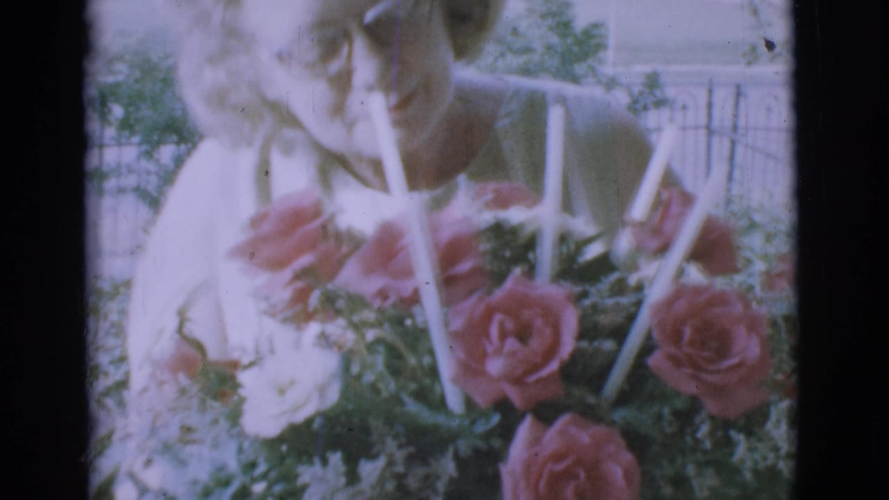 Older woman leans over a basket of pink and white roses with white candles outdoors.