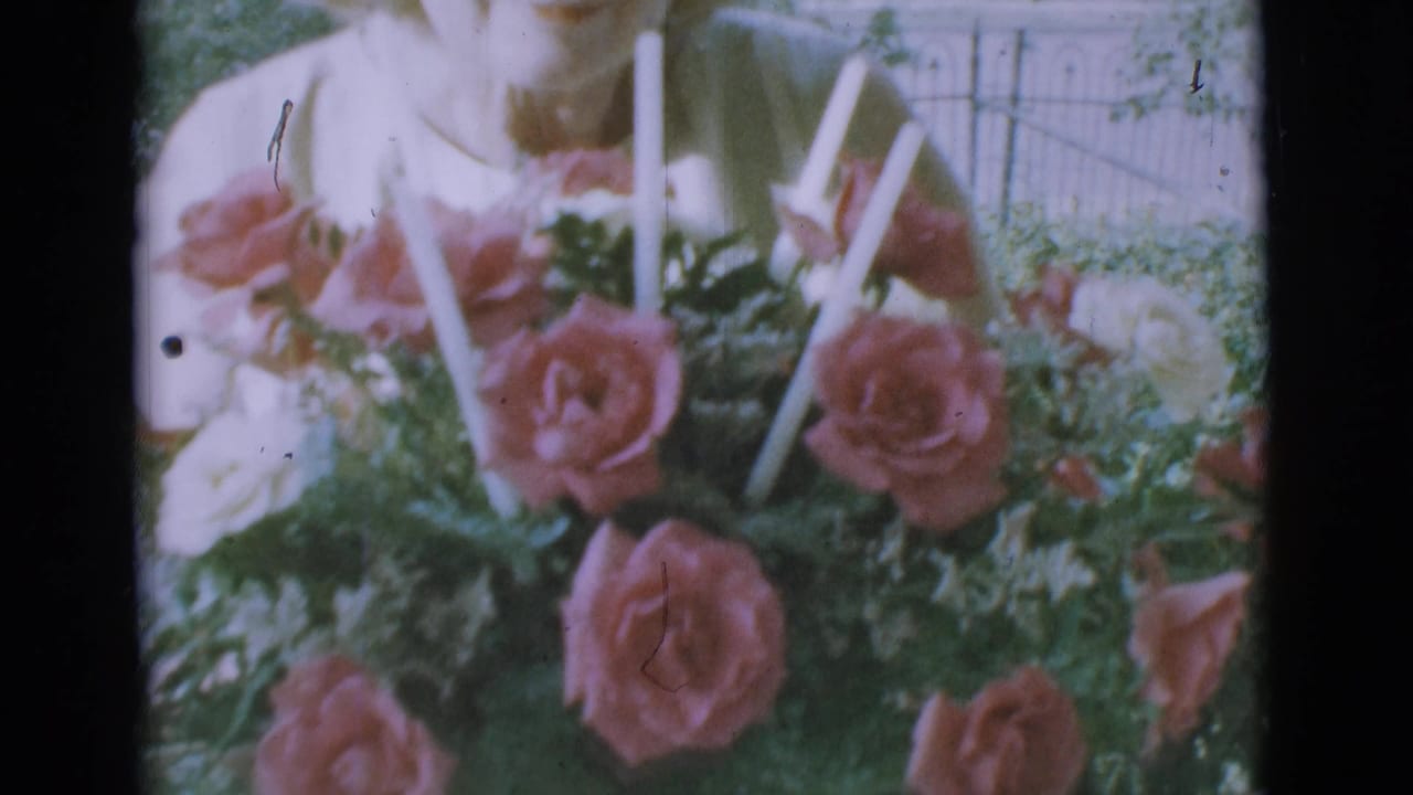 Basket bouquet of pink roses and white candles fills the frame with a woman partly visible behind it.