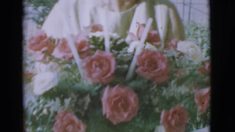 A close 8mm view shows pink and white roses, greenery, and candles, with the older woman's light dress behind the bouquet.