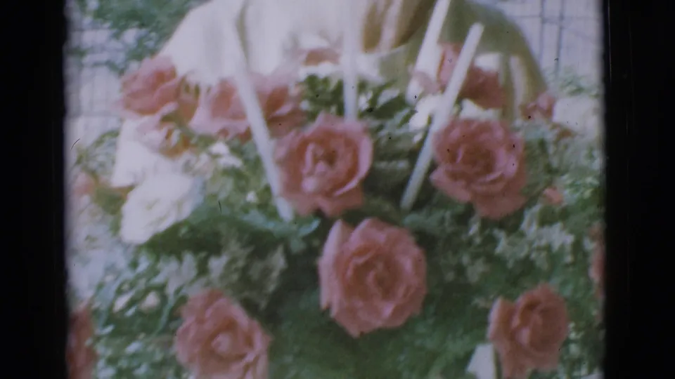 The final frame shows the candle-accented rose bouquet in soft focus, with the older woman leaning over it outdoors in Clarkdale.