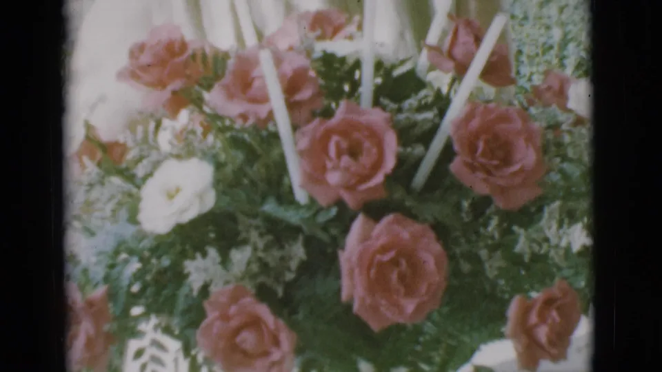 1966 Clarkdale, Arizona 8mm frame showing a close bouquet of pink roses, white flowers, ferns, and tall white candles on a porch.