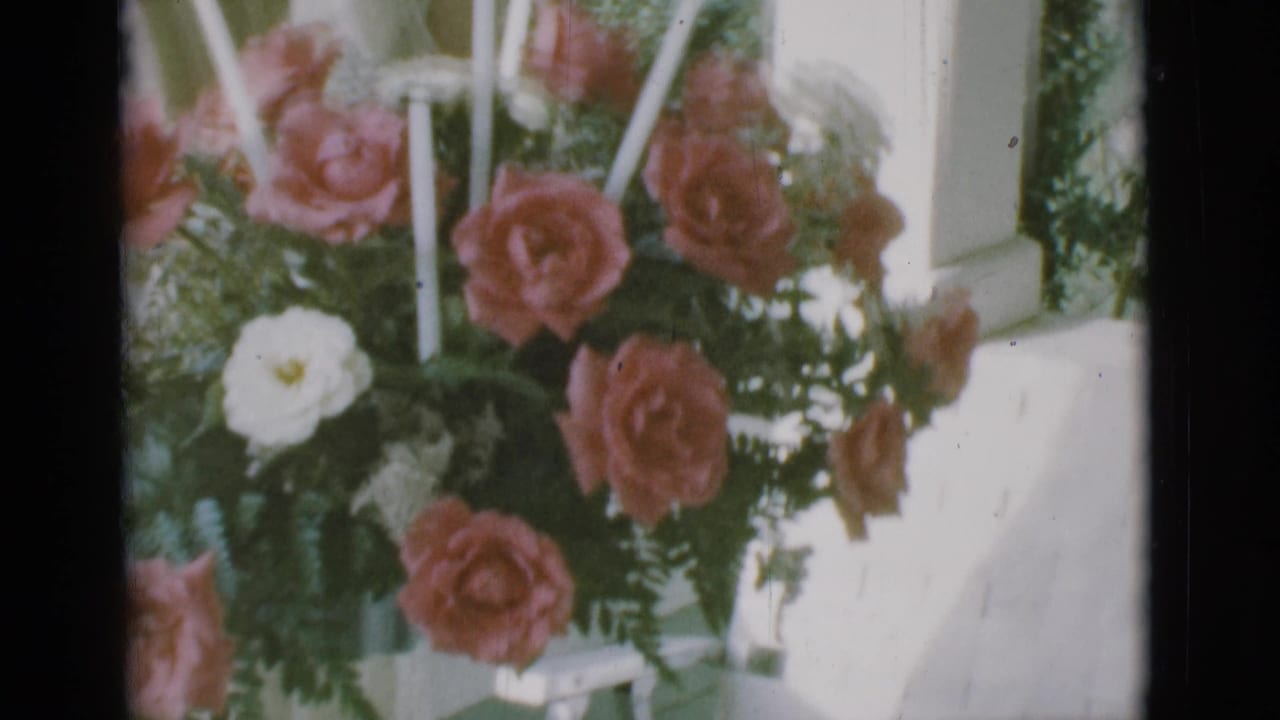 Bouquet with pink roses and white flowers beside porch siding and tall candles.