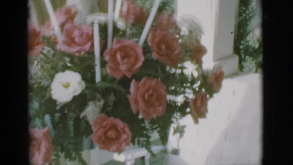 1966 Clarkdale, Arizona frame with pink roses, white blossoms, greenery, and white candles near exterior porch siding.