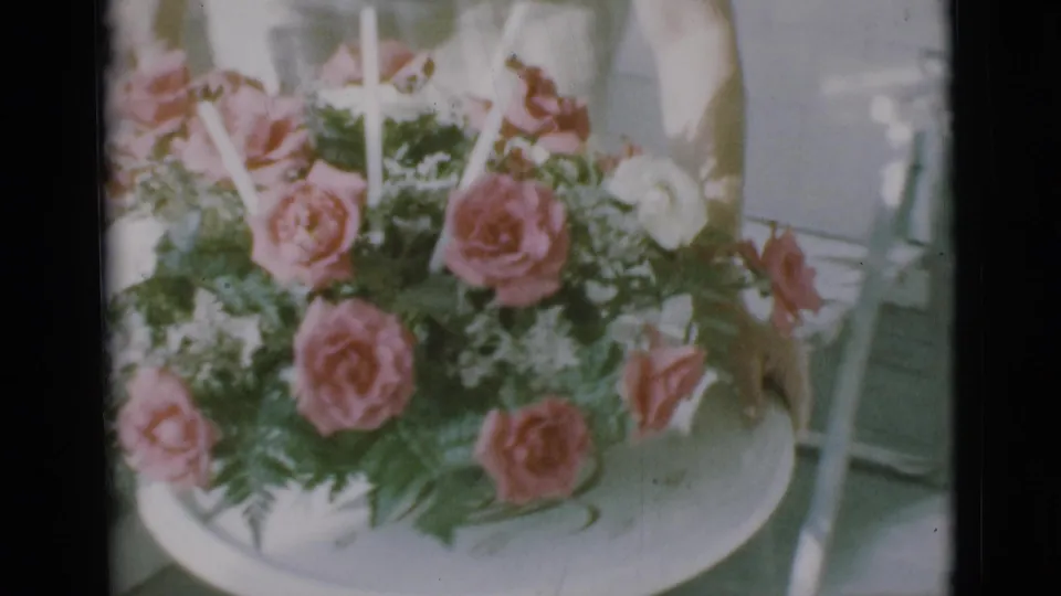 1966 Clarkdale home-movie frame of roses and greenery on a tray, with part of a light dress at the edge.
