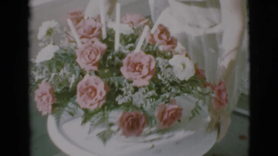 1966 Clarkdale frame showing hands near a pink and white rose arrangement in a white tray.