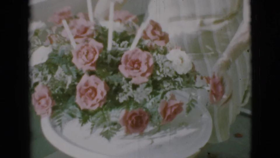 1966 Clarkdale 8mm still of a hand near a rose bouquet set in a white circular tray.