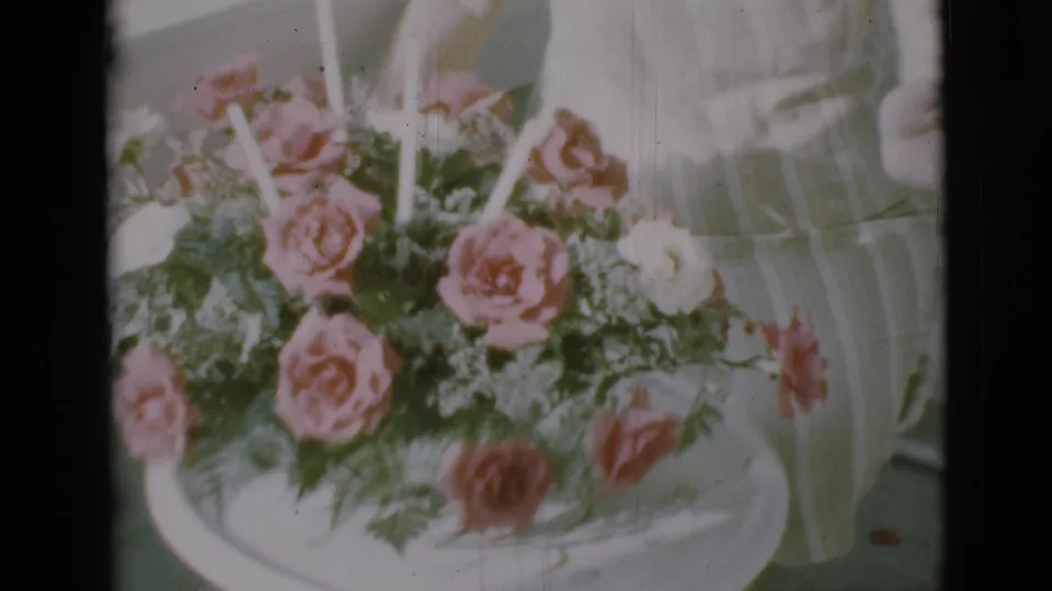1966 Clarkdale 8mm frame showing pink and white roses with green ferns in a white bowl, softly lit and slightly faded.