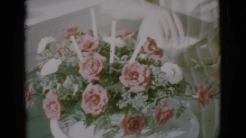 1966 Clarkdale 8mm frame with a hand near a rose bouquet, suggesting someone arranging or counting flowers.