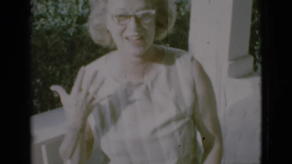 In 1966 Clarkdale home-movie footage, a woman in glasses smiles on a porch and gestures toward the camera.