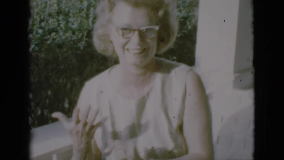 The woman remains on the porch in the Clarkdale 1966 clip, smiling near a white post with greenery behind her.